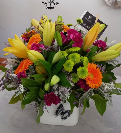 Heat Wave - A vibrant container arrangement, created using the fresh blooms of the day in a mix of orange, purple, yellow and green with complementary foliage.